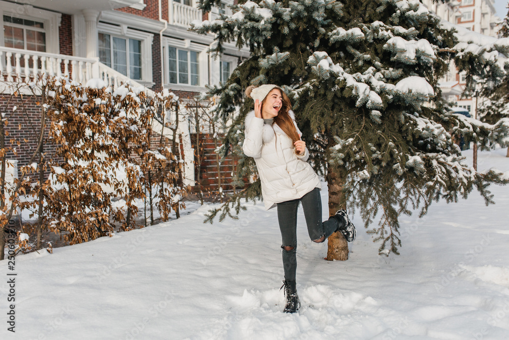 Charming tall girl in warm winter clothes having fun with snow on