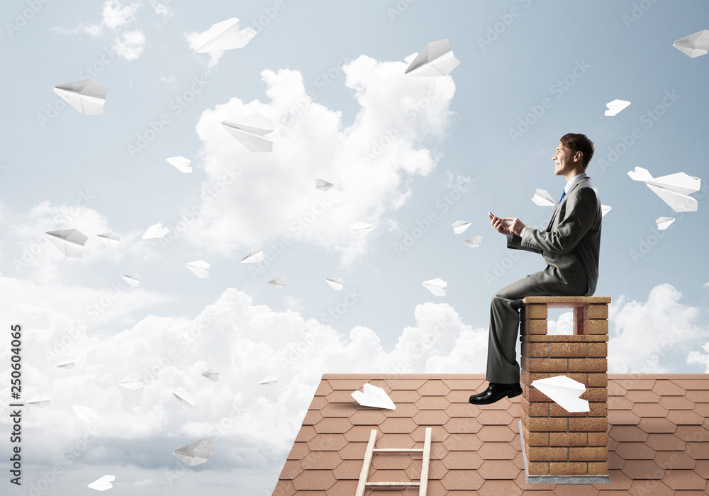 Man on brick roof send message with smartphone and paper planes flying in air Man on brick roof send message with smartphone and paper planes flying in air