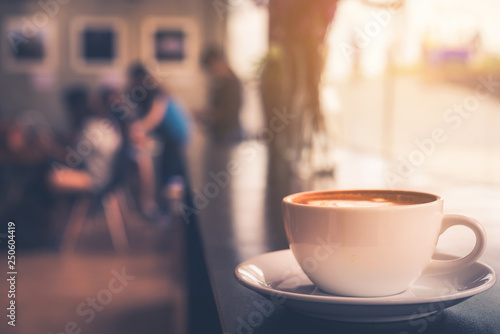 Cappuccino cup on the table with blur people in coffee shop background, vintage tone 