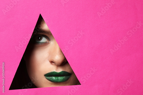 Beautiful young woman with bright makeup visible through triangle-shaped hole in color paper © Pixel-Shot