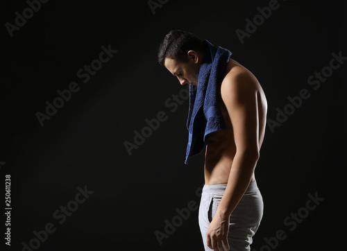 Sporty young man with towel against dark background