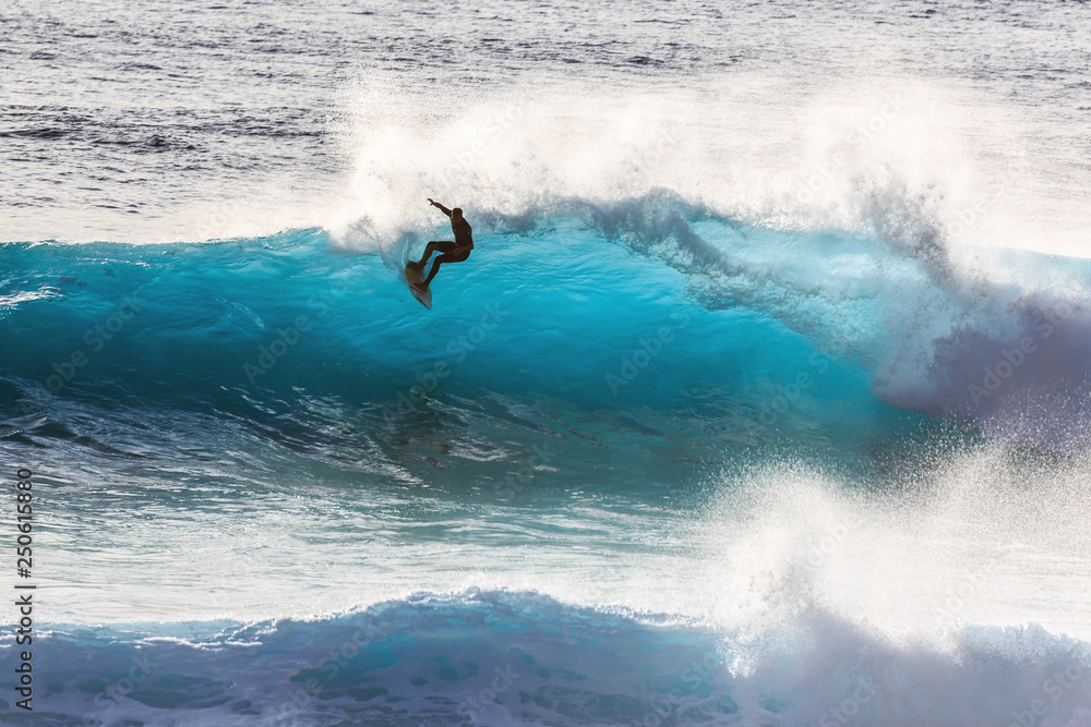 Silhouette surfer riding the big blue surf waves on the island Madeira, Portugal, a popular surfing tourist destination