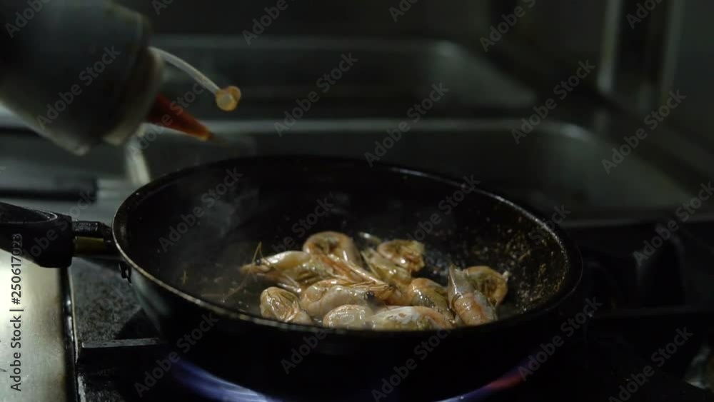 Сhef in the kitchen prepares shrimp on a hot pan sprinkling them with spices and pouring sauce Сhef in the kitchen prepares shrimp on a hot pan sprinkling them with spices and pouring sauce