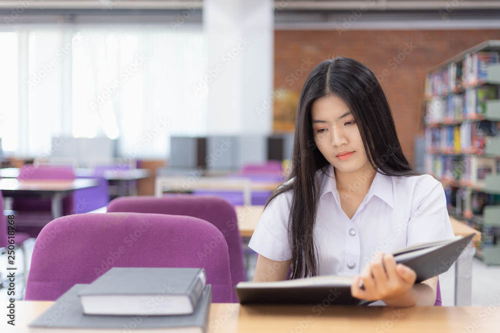 Asian woman is reading the book intently , she held the book and look at the ground in university library Asian woman is reading the book intently , she held the book and look at the ground in university library