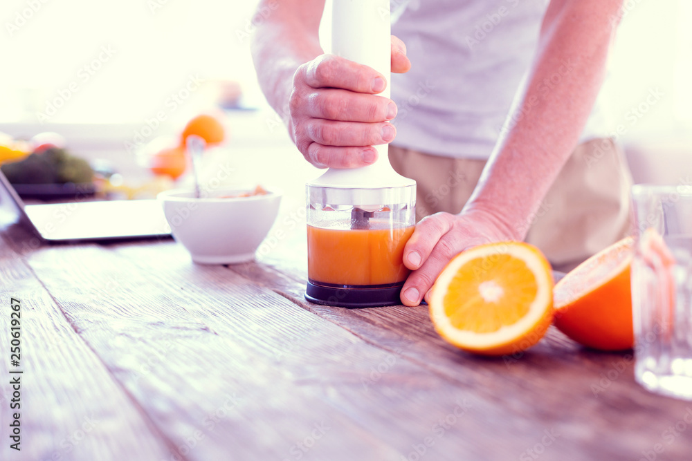Close up of man using his modern blender while squeezing morning orange juice Close up of man using his modern blender while squeezing morning orange juice