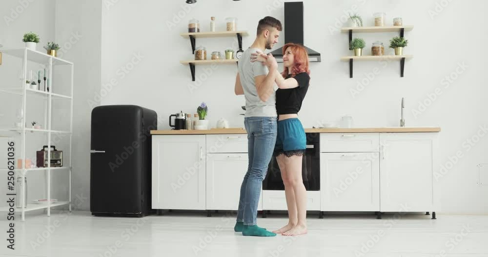 Happy young couple dancing in kitchen wearing pajamas listening to music morning at home Happy young couple dancing in kitchen wearing pajamas listening to music morning at home