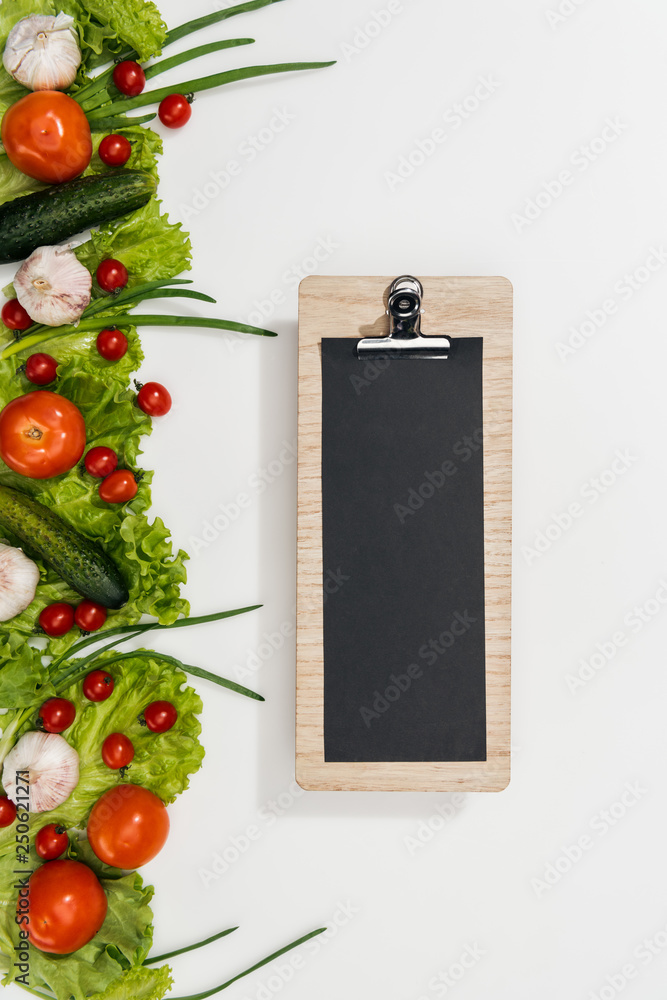 top view of empty clipboard with tomatoes, lettuce leaves, cucumbers, onion and garlic
