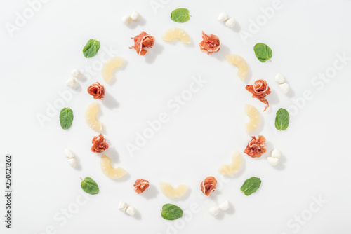 flat lay of delicious prosciutto near green basil leaves, sliced pineapples and mozzarella cheese on white background