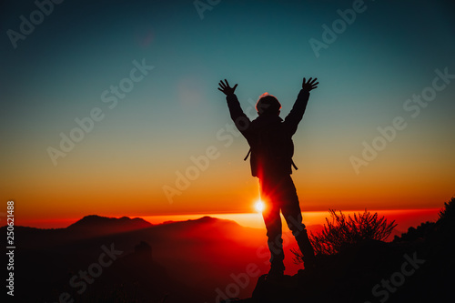Silhouettes of happy little boy hiking at sunset mountains