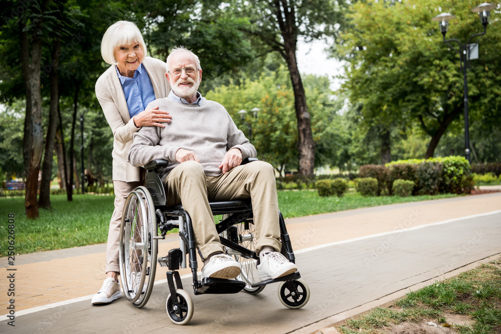 happy senior couple, smiling woman with husband in wheelchair in park happy senior couple, smiling woman with husband in wheelchair in park