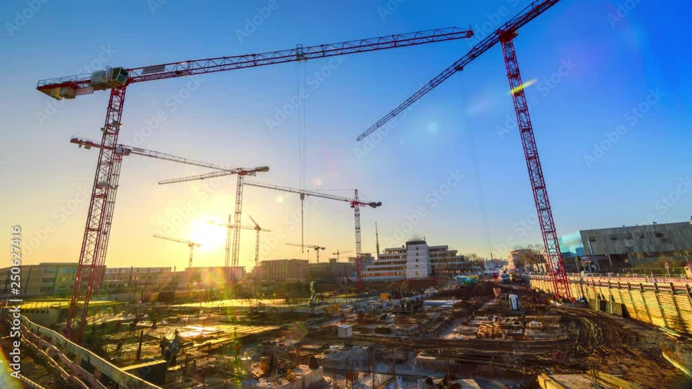 Timelapse footage of a large construction site with several busy cranes at dusk, with clear blue sky and the setting sun