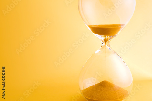 Hourglass with sand running through the bulbs on yellow background