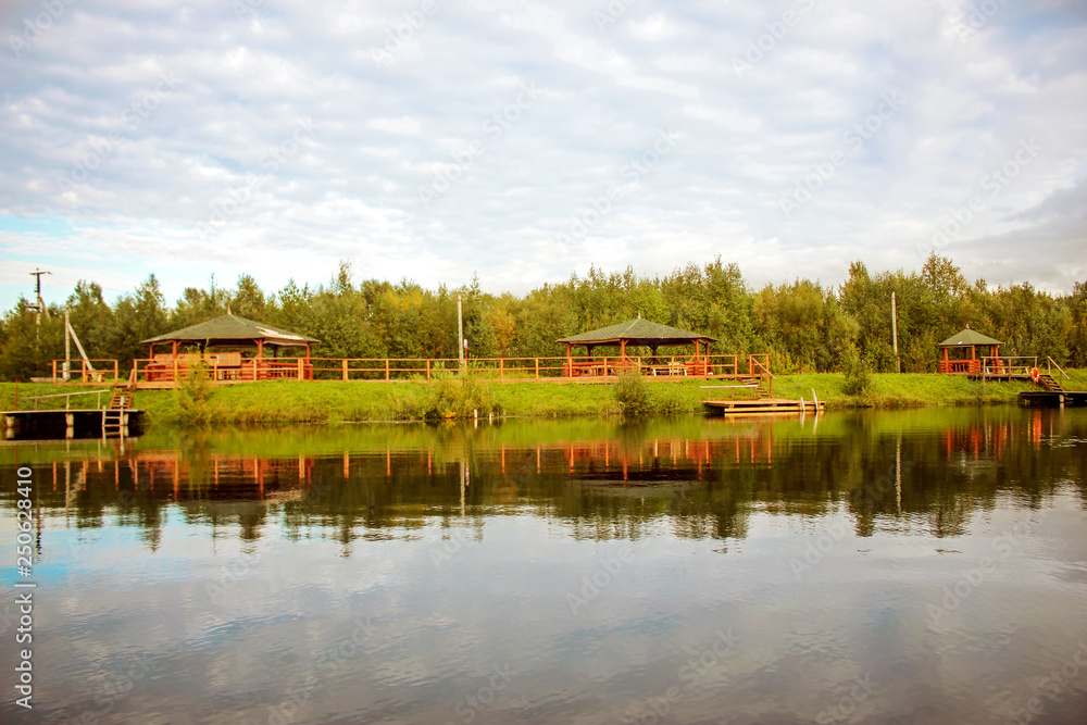 Wooden arbors are located above the surface of a picturesque lake. Sunny day, the sky is reflected in the water.