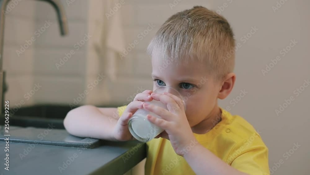 Closeup caucasian boy with big blue eyes drinking milk in the kitchen. Kid in yellow shirt. Boy smiling at the camera. mother wipes her sons mouth.