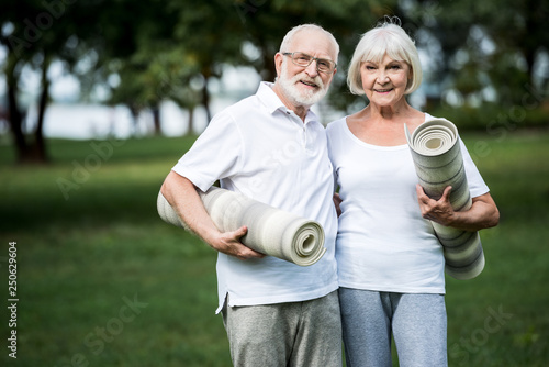 smiling senior couple embracing while holding fitness mats