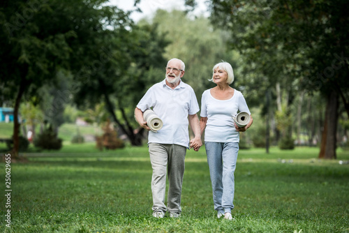 happy senior couple walking in park and holding fitness mats © LIGHTFIELD STUDIOS