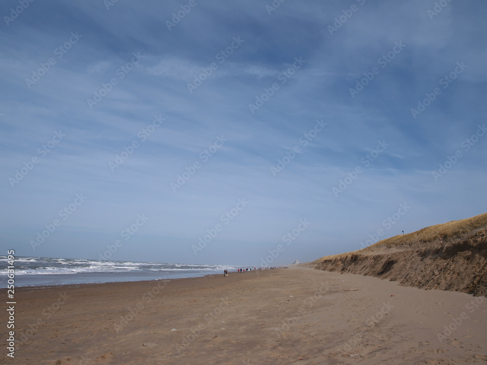 view down the beach of Katwijk with distant people. Noordwiijk at the horizon