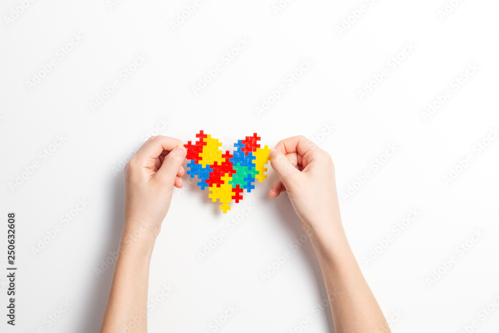 Child hands holding colorful heart on white background. World autism awareness day concept