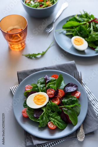 Salad mix with spinach, arugula,beet leaves, tomatoes and eggs on gray wooden background. Vegetarian food concept. Selective focus.