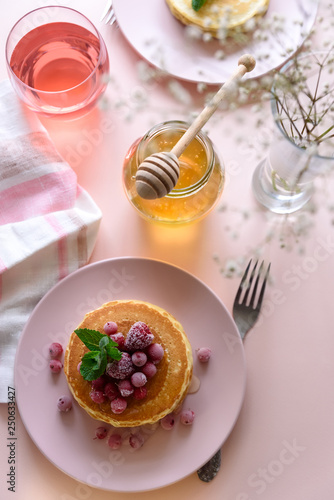 Stack of pancakes with frozen raspberry, red currant and honey on pink background. Selective focus