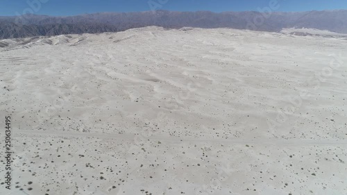 Aerial drone scene of desert with bright clear beige sand. Camera moving forwards discovering dunes and the andes mountains on background. Taton, Catamarca Province, Argentina. photo