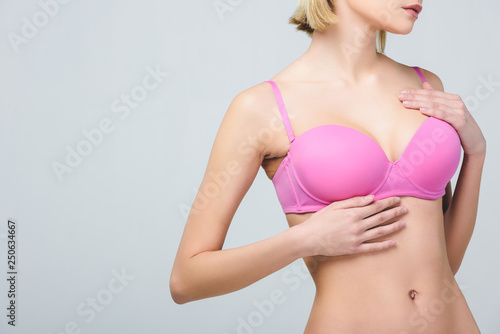 cropped view of woman in pink bra isolated on grey, breast cancer concept