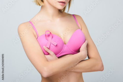 cropped view of girl with crossed arms in pink bra with breast cancer awareness ribbon, isolated on grey