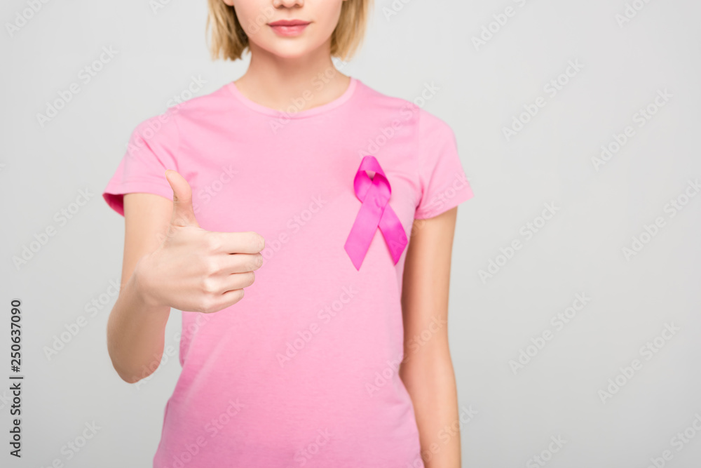 cropped view of young woman in pink t-shirt with breast cancer awareness ribbon showing thumbs up, isolated on grey cropped view of young woman in pink t-shirt with breast cancer awareness ribbon showing thumbs up, isolated on grey