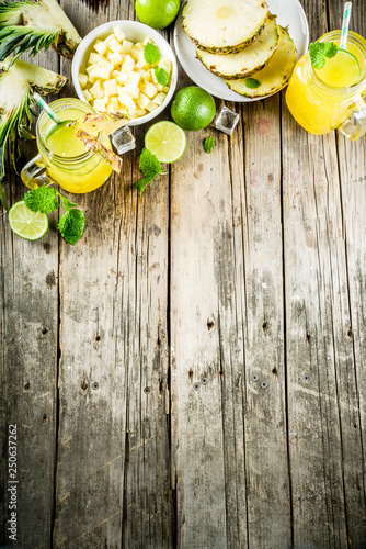 Cold pineapple mojito cocktail with ice, lime and mint, rustic wooden background copy space