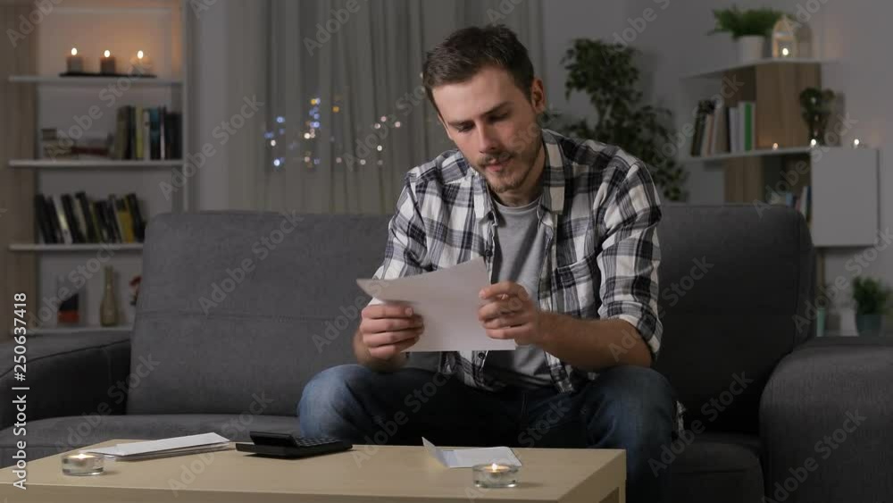 Confused man reading a letter sitting on a couch in the night at home