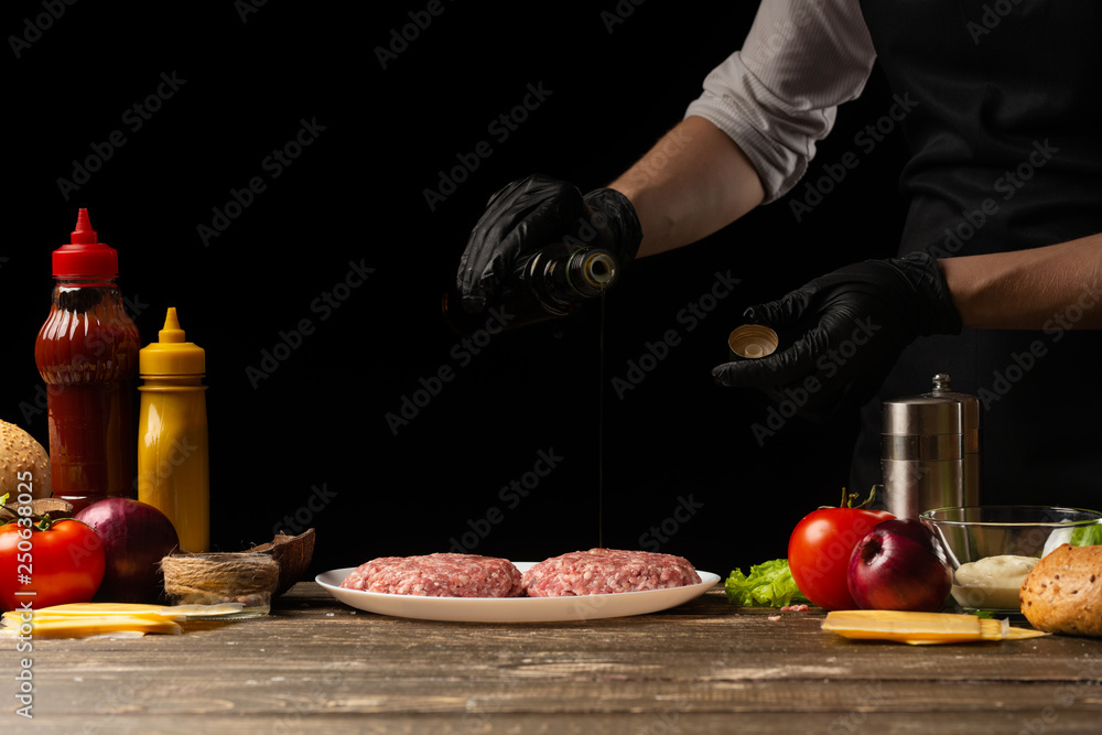 A cook prepares watering beef burgers with butter, on a background with ingredients, restaurant business, fast food, tasty food, gastronomy, cooking, menu
