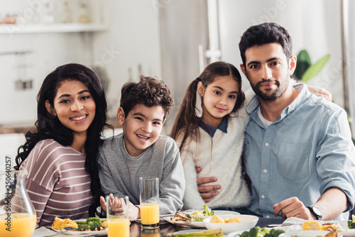 cheerful latin family hugging and looking at camera during lunch at home
