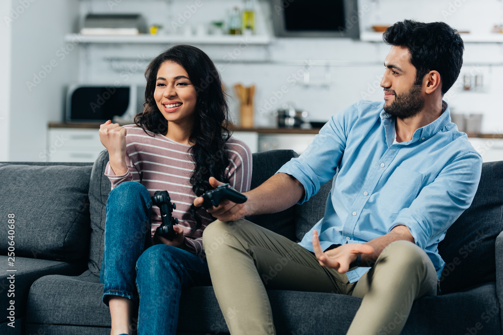 cheerful latin woman celebrating victory while holding joystick near husband after playing video game cheerful latin woman celebrating victory while holding joystick near husband after playing video game