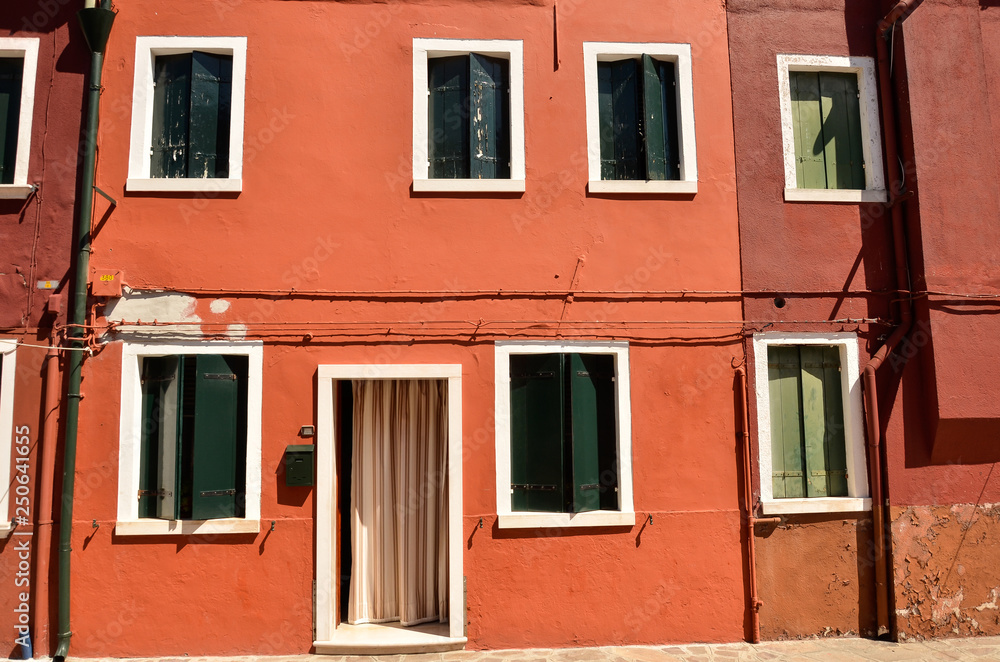 Windows with green shutters in Mediterranean style on orange wall. Colourful painted windows. Burano island near Venice, Italy. Abstract background, texture