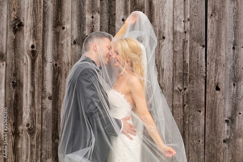 Bride and groom kissing undre veil in front of Barn Wood Wall photo