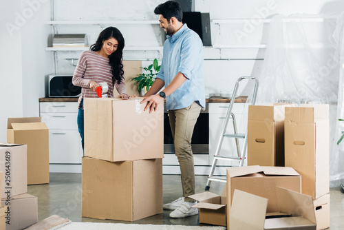Tablou pe pânză cheerful latin couple packing boxes while moving to new home