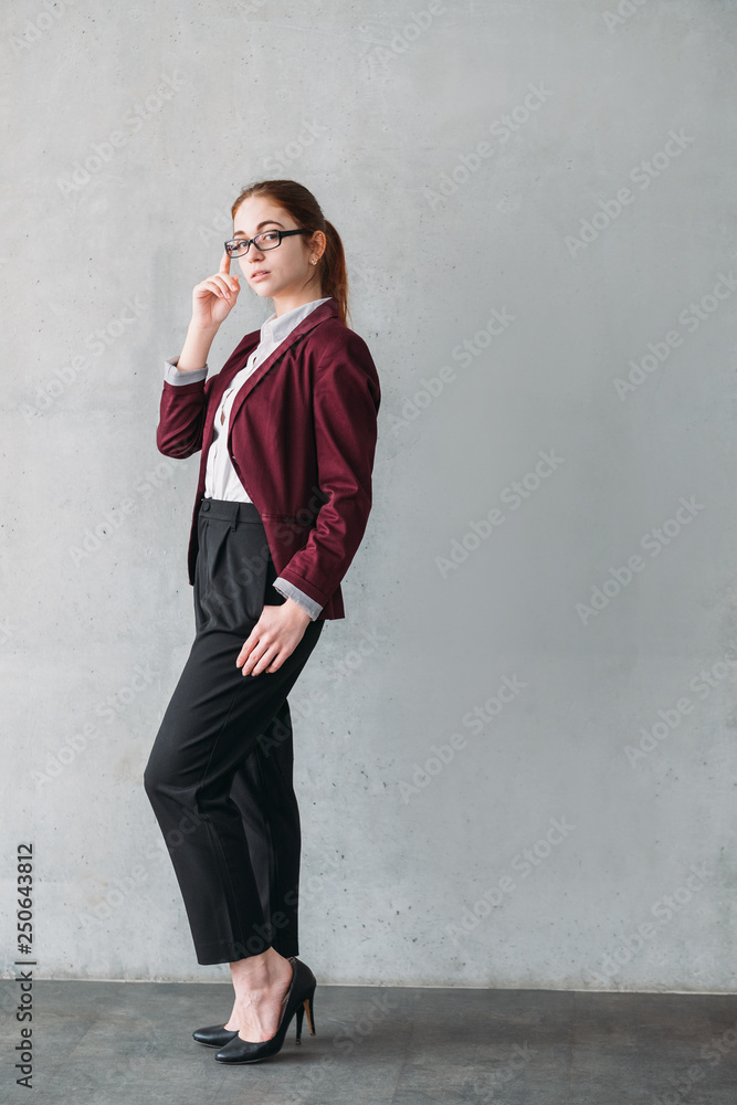 Confident teamlead. Successful career. Young business woman stand with hand at glasses. Copy space on grey background.