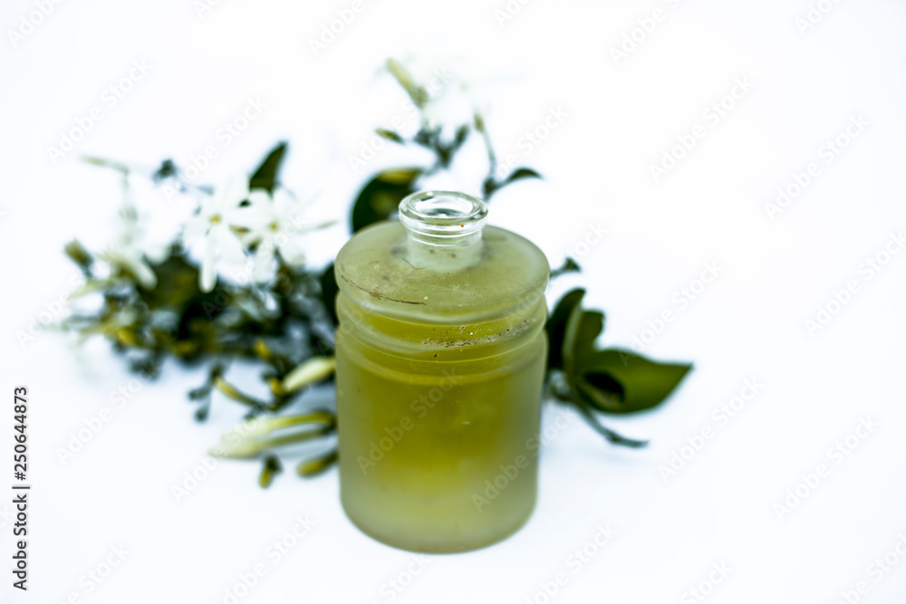 Close up of essential oil of Indian jasmine flower or juhi or Jasminum Auriculatum isolated on white in a small transparent glass bottle with raw flowers. Close up of essential oil of Indian jasmine flower or juhi or Jasminum Auriculatum isolated on white in a small transparent glass bottle with raw flowers.