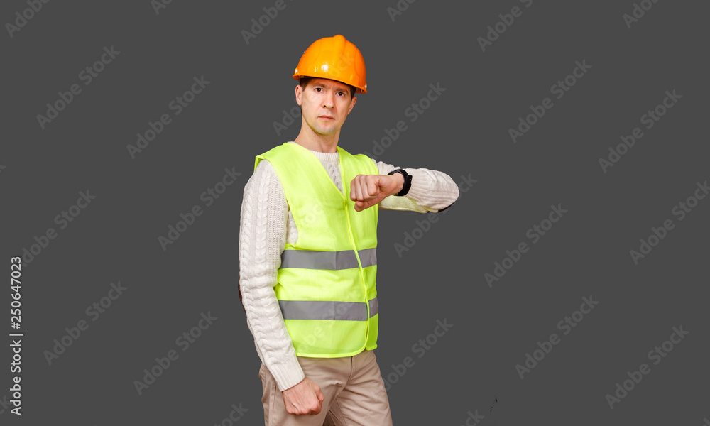 The man the builder in a helmet and a vest looks at the watch