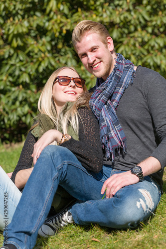 A happy young and loving couple sitting on a meadow in a park © StudioLaMagica