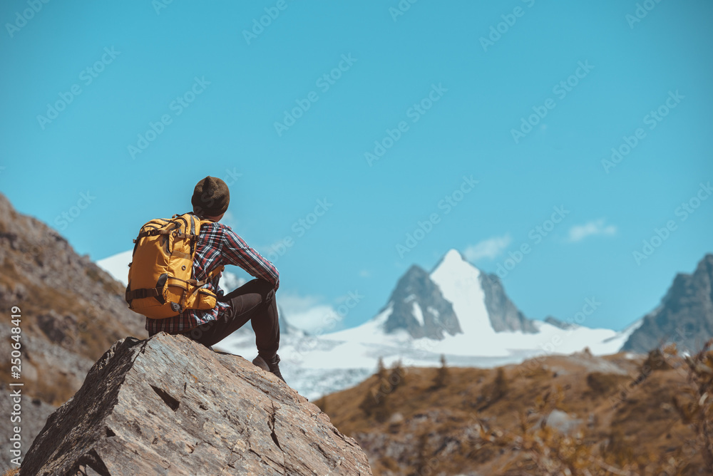 Hiker sits on big rock and looks at mountain