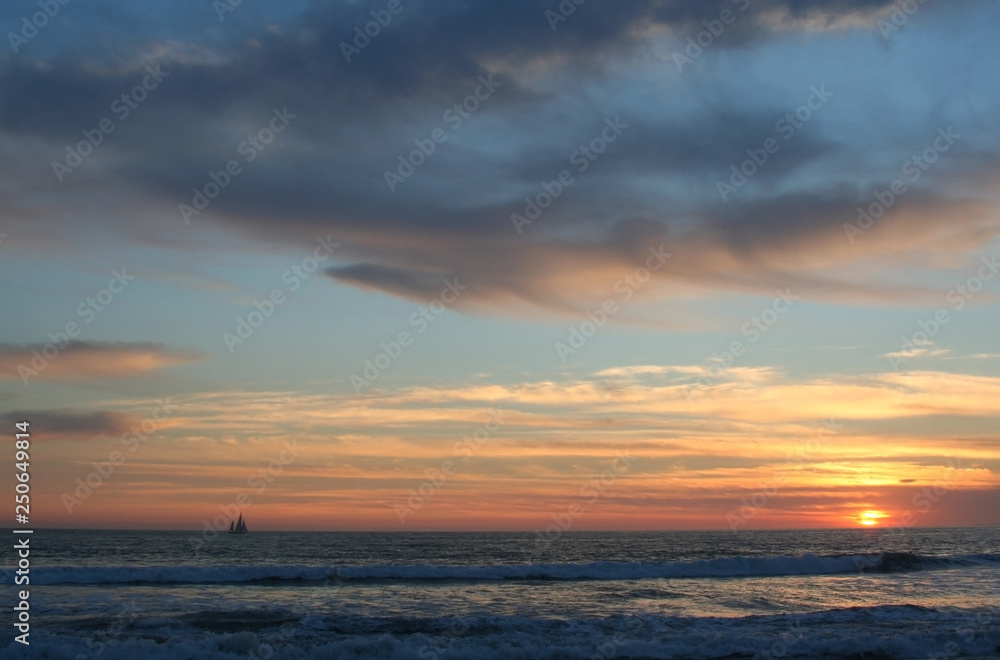 Lone sailboat crosses the horizon under a dramatic dusk sky
