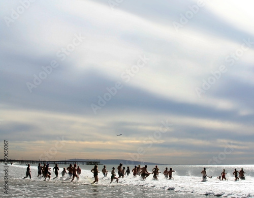Crowd of swimmers run into the ocean under a dramatic sky.