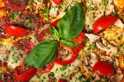 Close up Italian pizza with melted cheese, red cherry tomatoes, chicken, hen and fresh basil green leaves on a brown table decorated by mushrooms, red sweet pepper and cherry tomatoes
