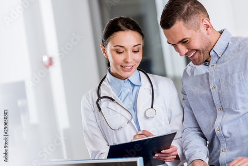Laughing doctor talking to patient and writing in clipboard