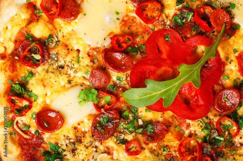 Close up Italian pizza with melted cheese, sausage, snack sticks, pepper and fresh green oregano leaves on a brown table decorated by mushrooms, red sweet pepper and cherry tomatoes