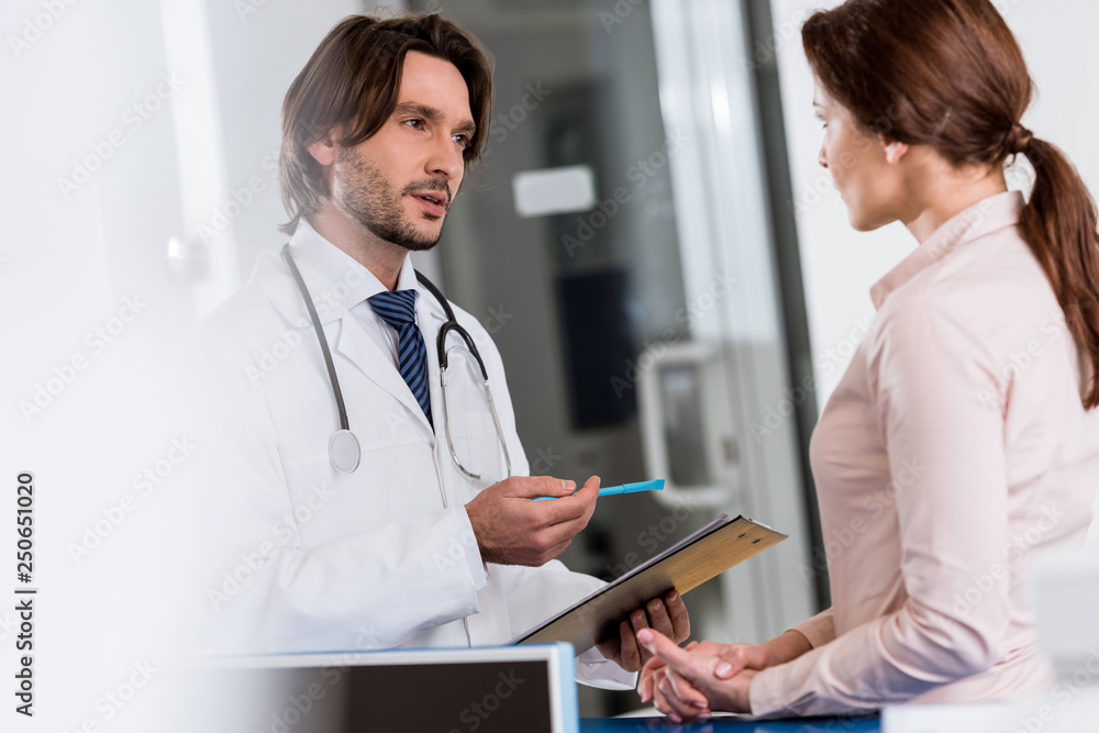 Doctor with clipboard talking to patient in clinic Doctor with clipboard talking to patient in clinic
