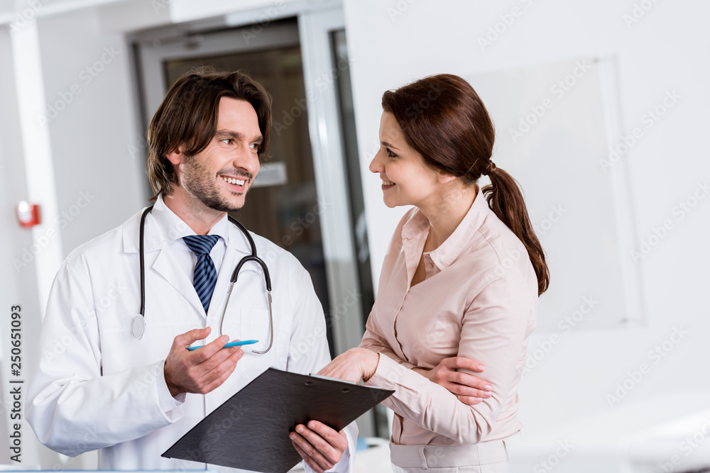 Handsome doctor holding clipboard and talking to patient in clinic Handsome doctor holding clipboard and talking to patient in clinic