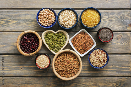 A set of various superfoods   whole grains beans  seeds  legumes in bowls on a wooden plank table. Top view  copy space.