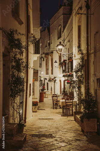 Fototapeta Naklejka Na Ścianę i Meble -  Narrow white street and restaurant tables in Locorotondo, region Puglia, Italy